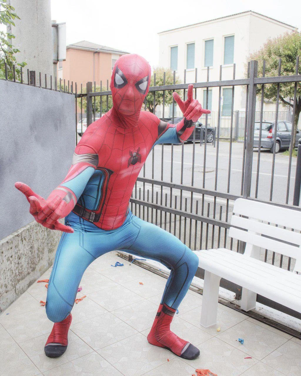 Costume di Spider-Man indossato da una persona in una posa da supereroe fuori da una recinzione in un'area urbana