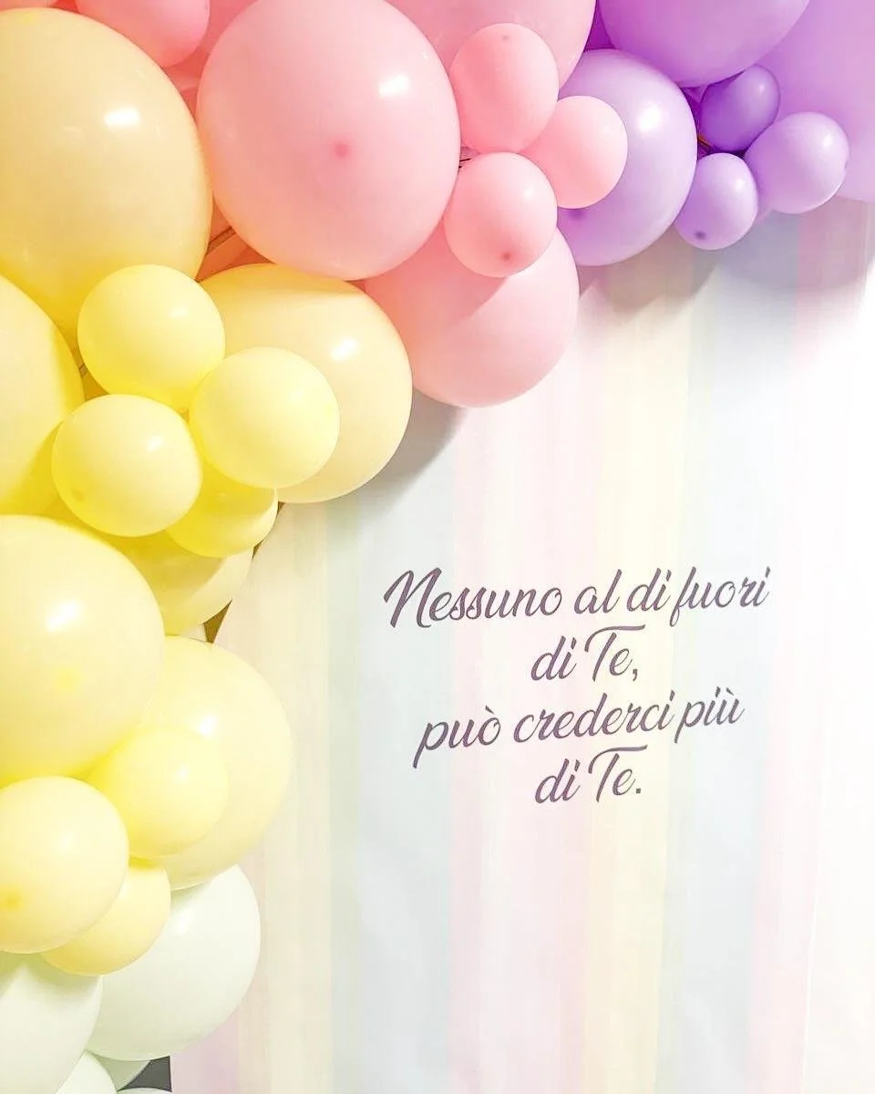 Decorazione con palloncini di vari colori pastello e una scritta in italiano.
