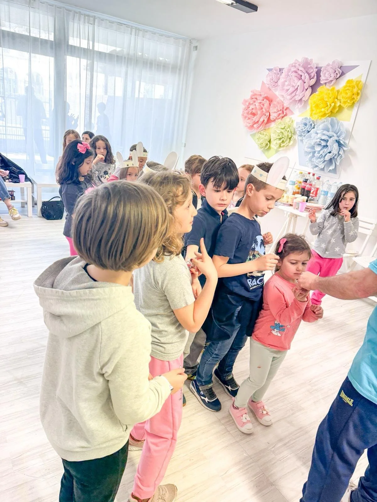 Bambini in fila che ricevono premi durante una festa di compleanno, con decorazioni colorate e un buffet sullo sfondo.