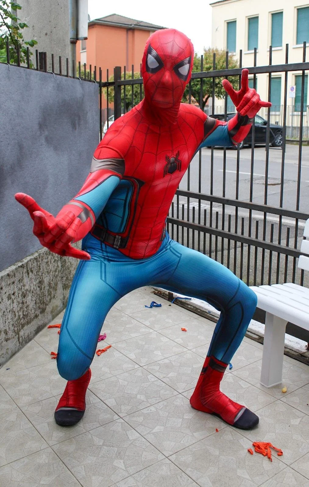 Persona vestita da Spider-Man in posa in uno spazio esterno con recinzione e edificio sullo sfondo.