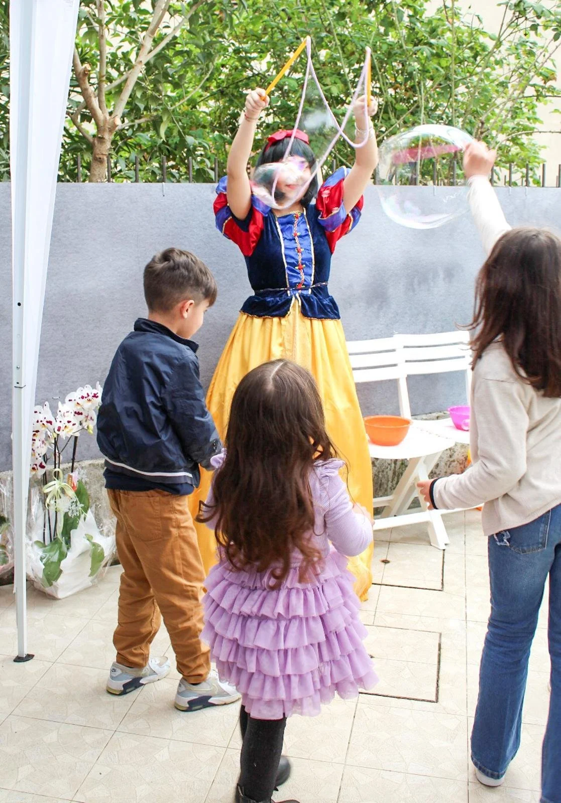 Bambina travestita da Bianca Snow White fa divertire bambini con bolle giganti durante una festa all'aperto.