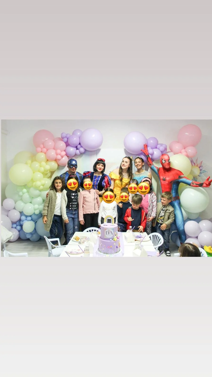 Festa di compleanno con bambini e adulti, decorazioni con palloncini color pastello e un grande dolce a due livelli con tema Spiderman, parete di sfondo con balloon a forma di nuvole di vari colori.