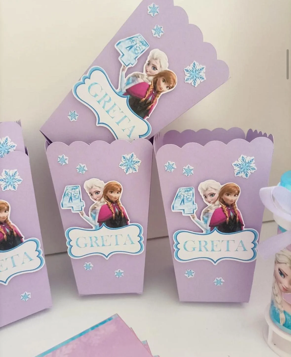 Confezioni di cartone color lilla con decorazioni di fiocchi di neve e adesivi di Elsa e Anna di Frozen. Ogni confezione ha il numero 4 e il nome Greta.