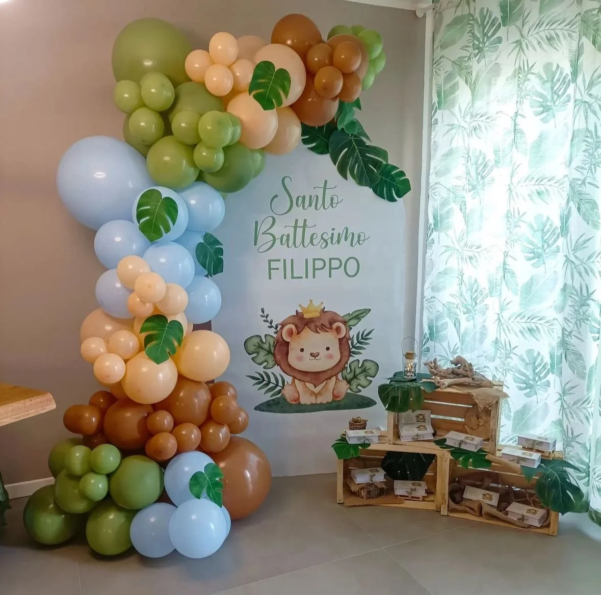 Decorazione per il battesimo di Filippo con palloncini nei toni del verde, beige, bianco e marrone, e un banner con un disegno di un leone con corona, foglie e testo "Santo Battesimo Filippo".
