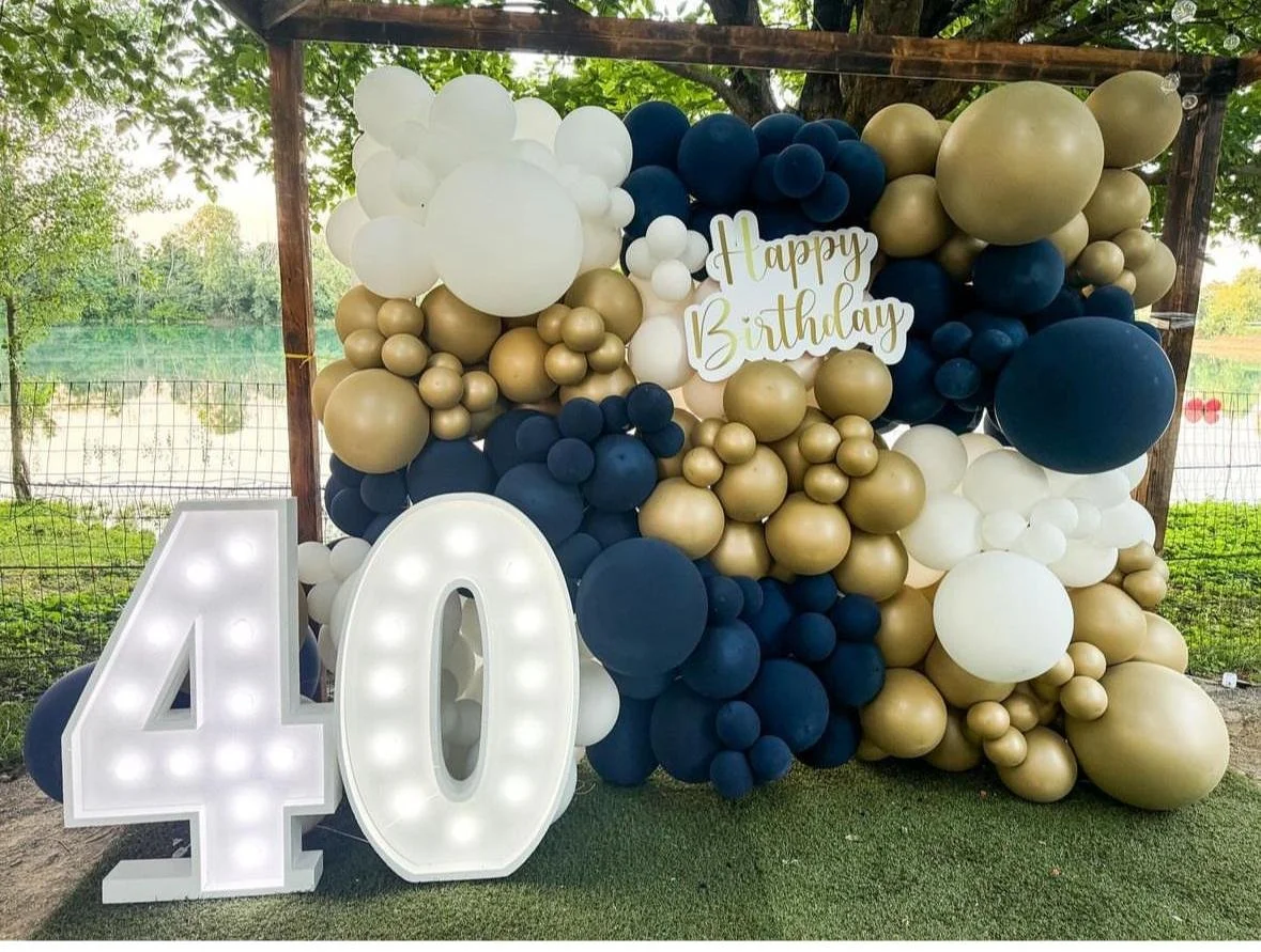 Decorazione di compleanno con palloncini bianchi, dorati e blu, una scritta 'Happy Birthday' e un numero 40 luminoso.
