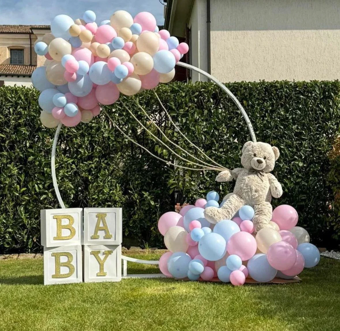 Decorazione per nascita con un orsetto di peluche e palloncini rosa, azzurri e bianchi, e blocchi con le lettere BABY.