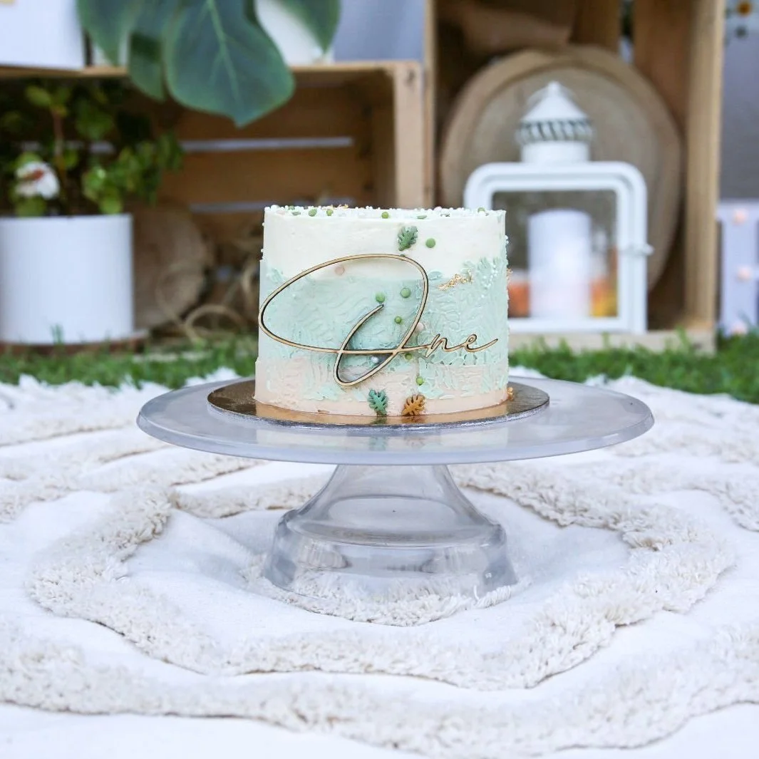Torta decorata con tema naturale, con scritta 'One' in un'ambientazione all'aperto.